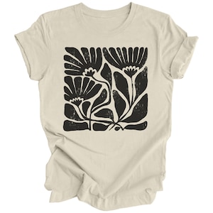 May include: A beige t-shirt with a black floral print. The print features stylized flowers and leaves in a block pattern.