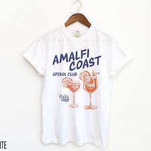 Puede incluir: Camiseta blanca con un estampado gr&aacute;fico de dos vasos de Aperol Spritz y el texto "Amalfi Coast Aperol Club Italia 1980".