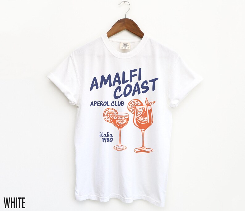 Puede incluir: Camiseta blanca con un estampado gr&aacute;fico de dos vasos de Aperol Spritz y el texto "Amalfi Coast Aperol Club Italia 1980".