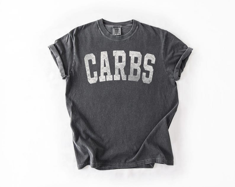 May include: Dark grey t-shirt with rolled sleeves. The word "CARBS" is printed in large, white, block letters across the front. The shirt is made of a soft, comfortable material.