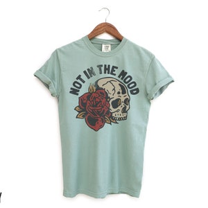 May include: A light blue t-shirt with a skull and rose graphic and the text "Not in the mood".