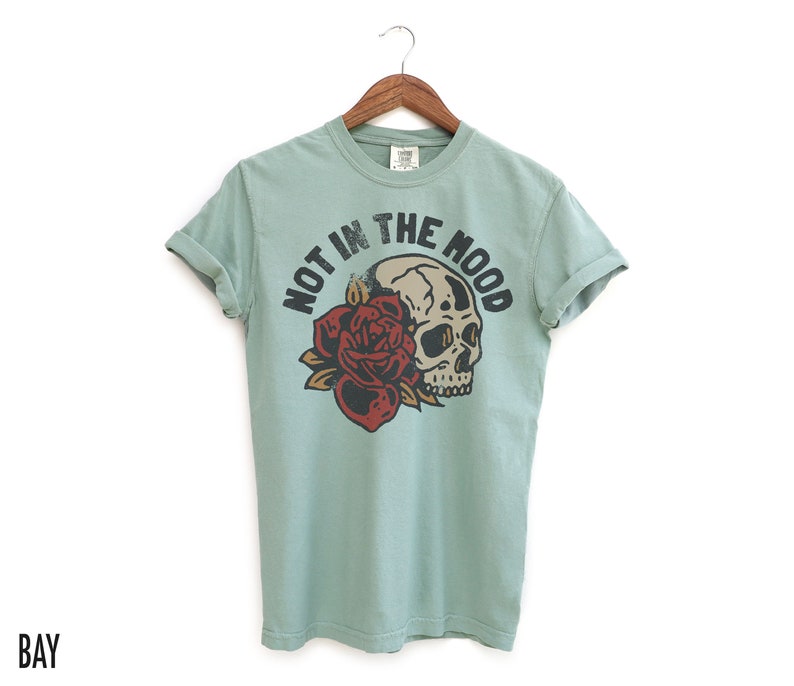 May include: A light blue t-shirt with a skull and rose graphic and the text "Not in the mood".