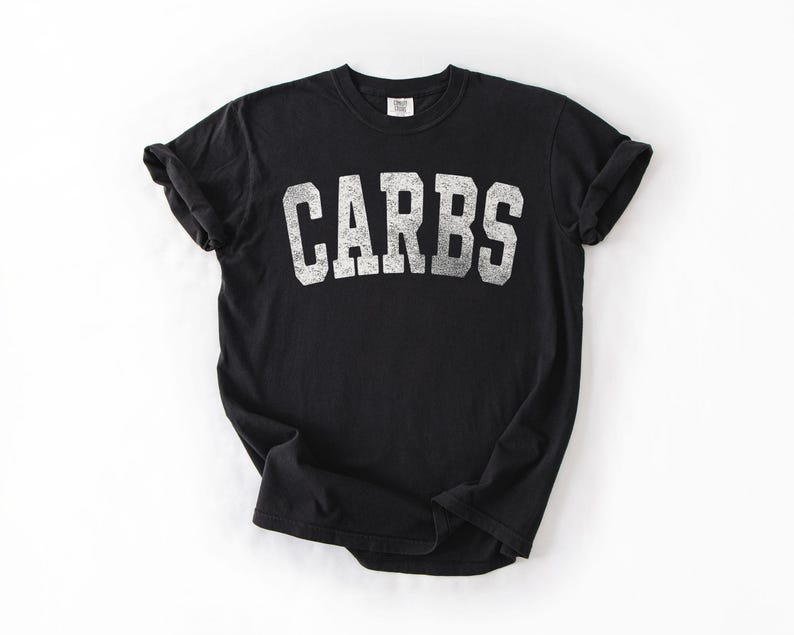 May include: Black t-shirt with the word "CARBS" printed in distressed white block letters. The shirt has short sleeves and a crew neck. The t-shirt is made of a soft material.
