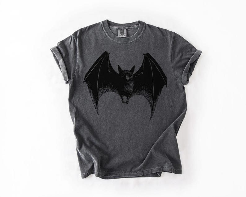 May include: Dark gray t-shirt featuring a black bat graphic with outstretched wings. The bat is centered on the shirt, with detailed wing and body features. The shirt has a vintage, worn look.