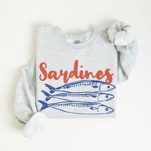 May include: A gray sweatshirt with the word "Sardines" printed in red and a graphic of three blue sardines.