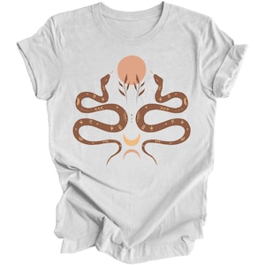 Puede incluir: Camiseta blanca con un dise&ntilde;o de serpiente marr&oacute;n. Las serpientes est&aacute;n entrelazadas y se miran. Hay un dise&ntilde;o de sol y luna en el centro de las serpientes.