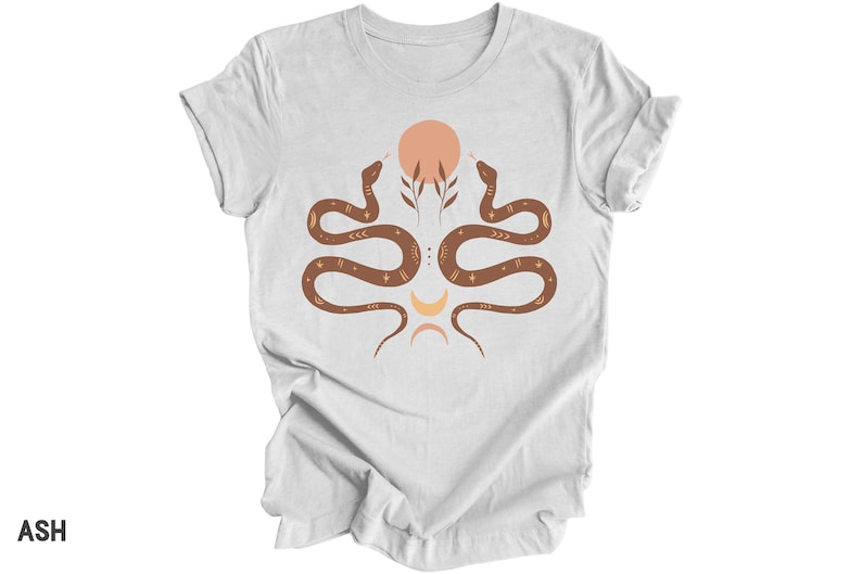 Puede incluir: Camiseta blanca con un dise&ntilde;o de serpiente marr&oacute;n. Las serpientes est&aacute;n entrelazadas y se miran. Hay un dise&ntilde;o de sol y luna en el centro de las serpientes.