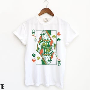 May include: White t-shirt featuring a green, orange and white illustration of a queen of hearts playing card with shamrocks.