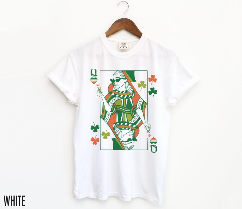 May include: White t-shirt featuring a green, orange and white illustration of a queen of hearts playing card with shamrocks.