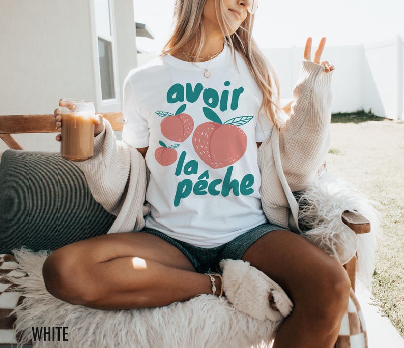 May include: White t-shirt with a graphic of peaches and the text "avoir la p&ecirc;che" in green and pink.