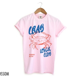 May include: Pink t-shirt with a blue and red graphic of a crab and the text "Crab Lover Club" and "Everyday All Day".