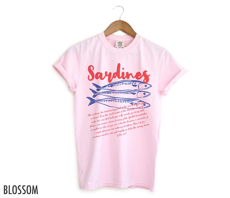 May include: Pink t-shirt with a blue and red illustration of sardines and the text "Sardines" in red. The text below the illustration reads "Oh, witness the  discerning palates of the discerning... a descent from the world waters of the Mediterranean... a diet... from the world's only source of being bold... where the waves build their sandy paths... Got it? You're a...  a simple pleasure and a handsomely presented...  a mouthful of goodness and culinary finesse... a reminder of...  a simple pleasure and a mighty mouthful... the messy...  sardines will go on forever in our hearts...  of the sea!"