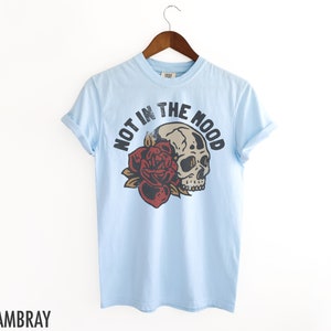 May include: Light blue t-shirt with a skull and rose graphic and the text "NOT IN THE MOOD".