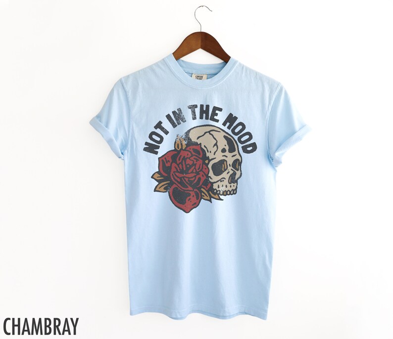 May include: Light blue t-shirt with a skull and rose graphic and the text "NOT IN THE MOOD".