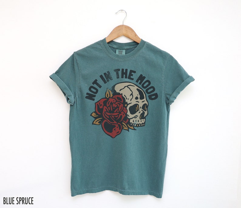 May include: Teal blue t-shirt with a skull and rose graphic and the text "Not in the Mood".