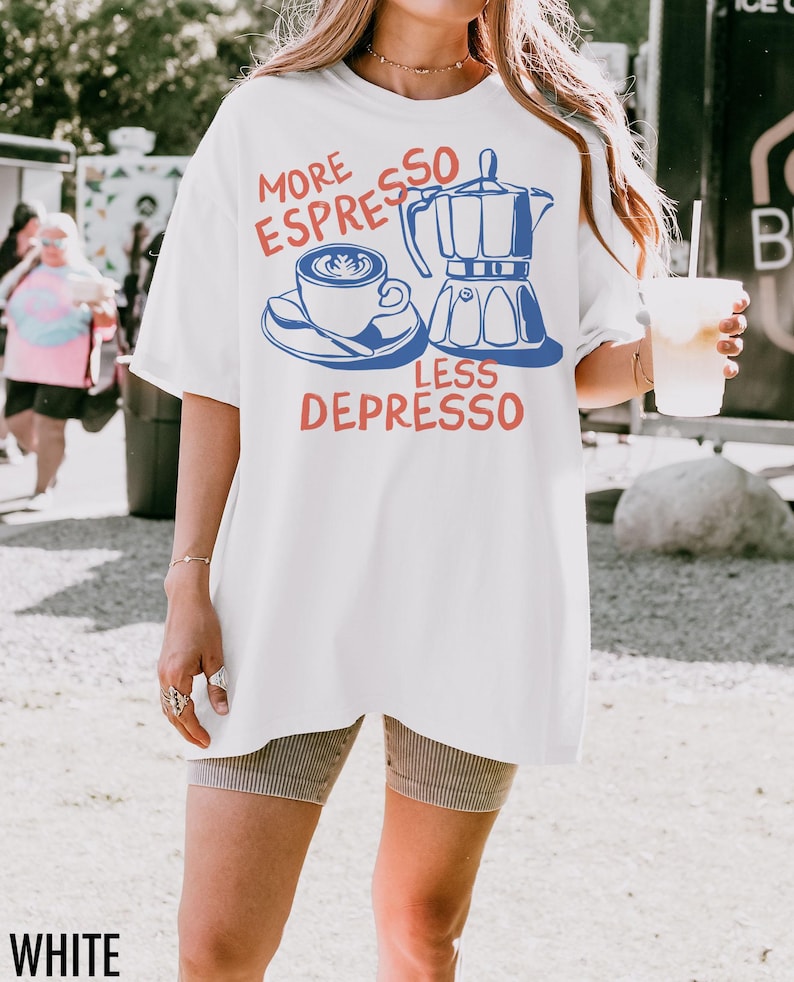 May include: White t-shirt with a blue and red graphic. The graphic features a coffee cup, a stovetop espresso maker, and the text "MORE ESPRESSO LESS DEPRESSO". The shirt is a casual, oversized style.