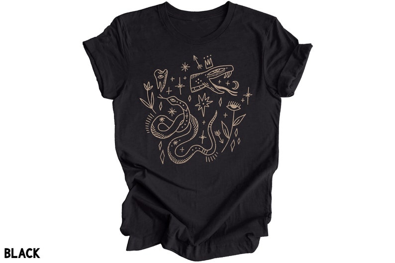Puede incluir: Camiseta negra con un gr&aacute;fico de contorno dorado de una serpiente, una corona, un ojo, un diente y estrellas.