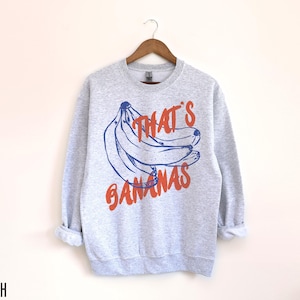 K&ouml;nnte beinhalten: Ein graues Sweatshirt mit einer blauen und orangenen Grafik von Bananen und dem Text "That's Bananas".