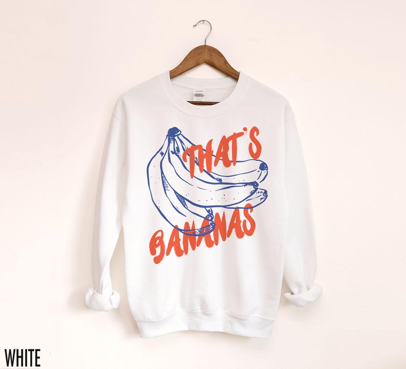 K&ouml;nnte beinhalten: Wei&szlig;er Pullover mit einer blauen und orangenen Grafik von Bananen und dem Text "That's Bananas".