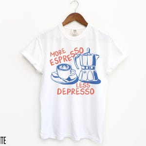 May include: White t-shirt with a blue and red graphic that says "More Espresso Less Depresso". The graphic features a cup of coffee and a coffee pot.