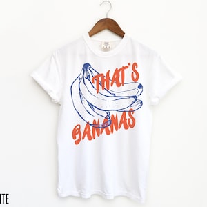 Pu&ograve; includere: Maglietta bianca con una grafica blu e arancione di banane e il testo "That's Bananas".