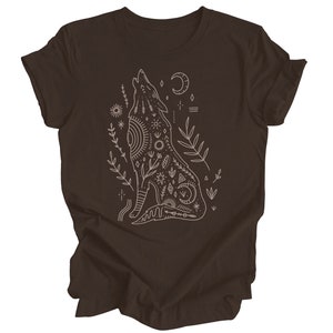 May include: A brown t-shirt with a white outline of a wolf howling at the moon. The wolf is surrounded by floral designs and geometric patterns.