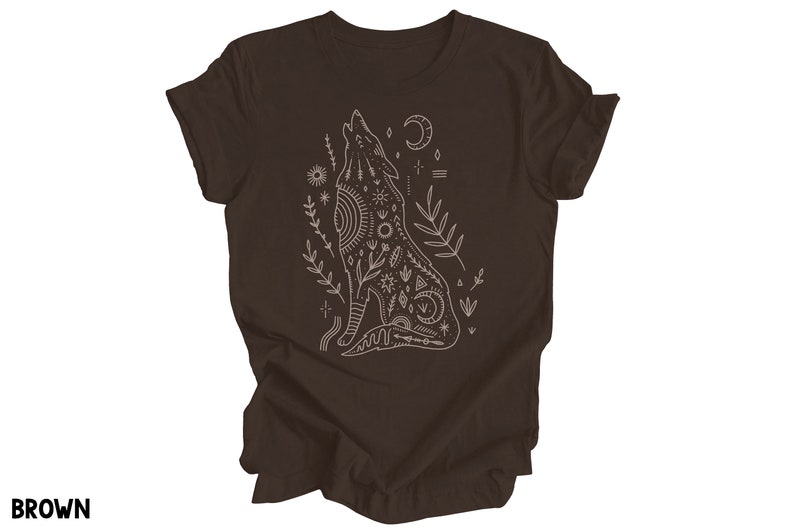 May include: A brown t-shirt with a white outline of a wolf howling at the moon. The wolf is surrounded by floral designs and geometric patterns.
