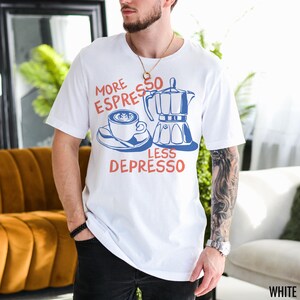 May include: White t-shirt with a blue and red graphic of a coffee pot and a cup of coffee. The text on the shirt reads "More Espresso Less Depresso".