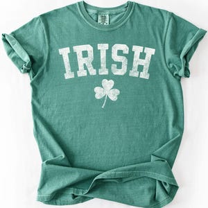 May include: A green t-shirt with the word "IRISH" in large, distressed white letters and a white shamrock below. The shirt has a crew neck and short sleeves, perfect for St. Patrick's Day or showing Irish pride.