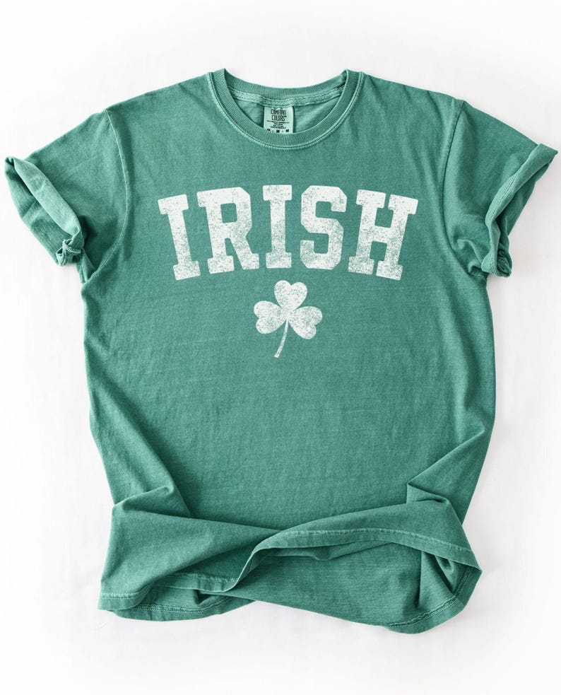 May include: A green t-shirt with the word "IRISH" in large, distressed white letters and a white shamrock below. The shirt has a crew neck and short sleeves, perfect for St. Patrick's Day or showing Irish pride.