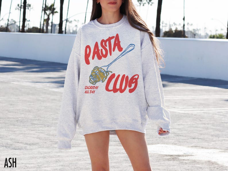 May include: A gray sweatshirt with the text "PASTA CLUB" in red and blue. The text "EVERYDAY ALL DAY" is printed in smaller red letters below the main text. A blue and white illustration of a fork with pasta on it is shown above the text.