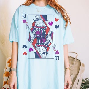 May include: A light blue t-shirt with a graphic of the Queen of Hearts playing card. The Queen is wearing sunglasses and a crown. The card is surrounded by hearts.
