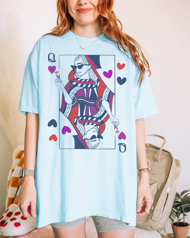 May include: A light blue t-shirt with a graphic of the Queen of Hearts playing card. The Queen is wearing sunglasses and a crown. The card is surrounded by hearts.