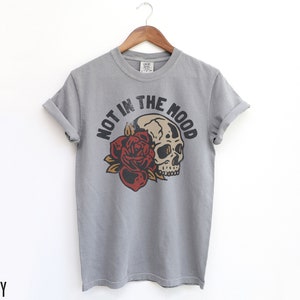 May include: Grey t-shirt with a skull and rose graphic and the text "Not in the Mood".