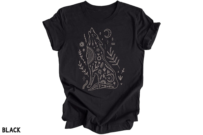 Puede incluir: Camiseta negra con un dibujo lineal de un lobo aullando con una luna creciente y otros s&iacute;mbolos celestiales. El lobo est&aacute; rodeado de plantas estilizadas.