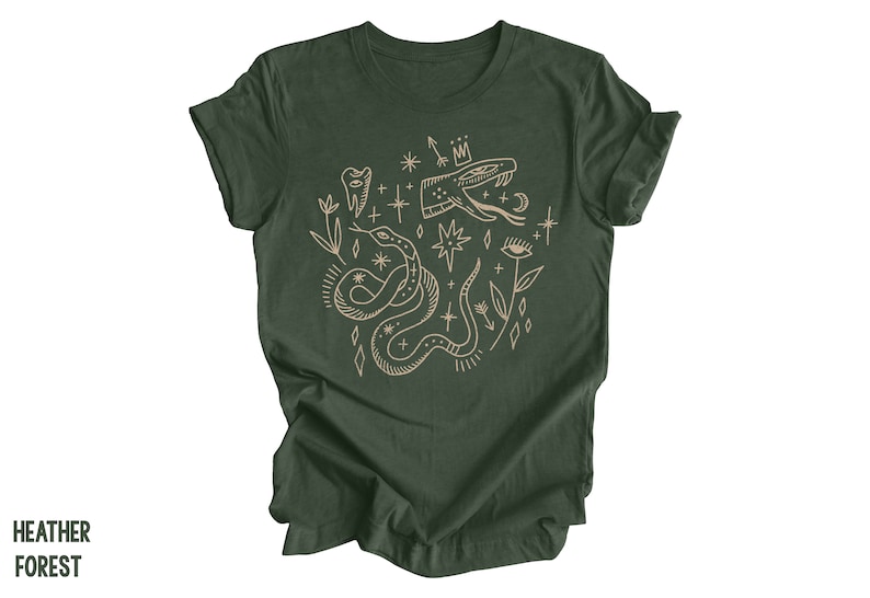 Puede incluir: Una camiseta verde oscuro con un estampado gr&aacute;fico beige de una serpiente, estrellas y otros s&iacute;mbolos m&iacute;sticos.