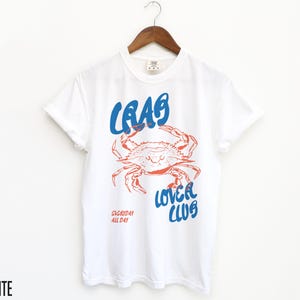 May include: White t-shirt with a blue and red graphic of a crab with the text "Crab Lover Club" and "Everyday All Day" printed on the front.