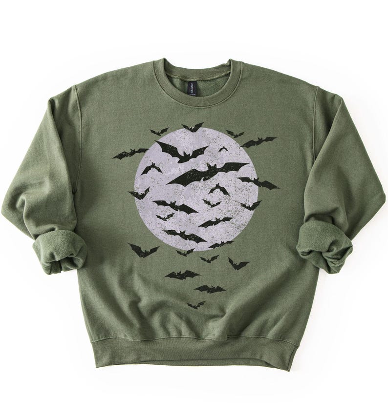 May include: An olive green sweatshirt with a distressed graphic of a full moon and black bats. The design is on the front of the crew neck top. The long-sleeved sweatshirt has a relaxed fit and rolled sleeves. A Halloween-themed garment.