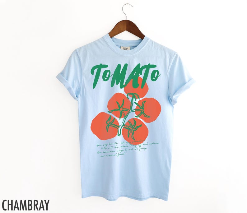 May include: Light blue t-shirt with a green "TOMATO" graphic and a drawing of red tomatoes on a vine. The text below the tomatoes reads "Their very soul. We're to the whole world. If we help will make the whole world off the page. The deliciousness is not to the fussy, unseasoned fruit."