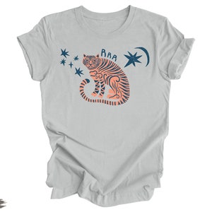 Peut inclure: Un t-shirt gris clair avec un motif de tigre rose &agrave; rayures bleues, une lune croissante et des &eacute;toiles. Le texte "RAA" est au-dessus du tigre.