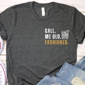 May include: A dark gray t-shirt with the text "CALL ME OLD FASHIONED." in white with a graphic of a glass of whiskey in gold.