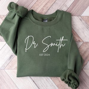 May include: A dark green sweatshirt with the text "Dr. Smith EST 2024" in white.