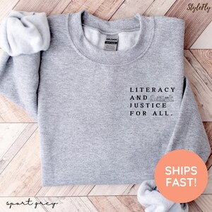 Puede incluir: Sudadera gris deportiva con el texto "LITERACY AND JUSTICE FOR ALL" en negro. La sudadera tiene cuello redondo y mangas largas. Tambi&eacute;n son visibles las palabras "StyleFly" y "sport grey".