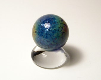 May include: A blue glass marble with iridescent flecks and a textured surface, displayed on a clear glass stand.