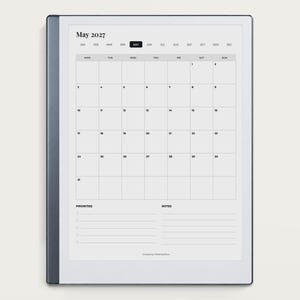 May include: A digital tablet displaying a May 2027 monthly calendar page. The screen features a grid layout with days of the week, numbered dates, and sections for priorities and notes at the bottom. The device has a dark gray frame.