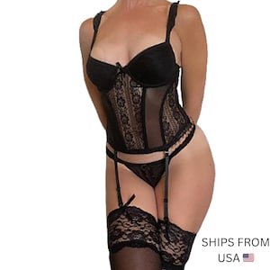 Op de afbeelding: Zwarte lingerie set met een kanten corset met verstelbare bandjes, een bijpassende string en jarretels. De set bevat dijhoge kousen met kanten rand. Het corset heeft een doorschijnend mesh paneel.