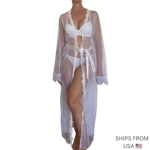Peut inclure: Un peignoir blanc transparent arrivant jusqu'aux pieds, doté de manches longues avec des poignets en dentelle, d'une ouverture avant bordée de dentelle et d'un ruban en satin blanc assorti à la taille. Porté sur un ensemble soutien-gorge et culotte.
