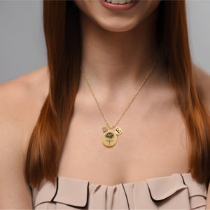 Pu&ograve; includere: Una collana d'oro con una catena delicata e un ciondolo rotondo con un motivo floreale. Il ciondolo ha anche un piccolo ciondolo con la lettera 'E' su di esso.