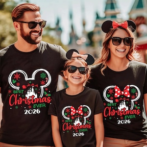 May include: Three black t-shirts featuring a white Mickey Mouse ear silhouette graphic. The design includes a castle, Santa's sleigh, snowflakes, and the red text "BEST CHRISTMAS EVER 2026". The shirts for the two females include a red polka dot bow.