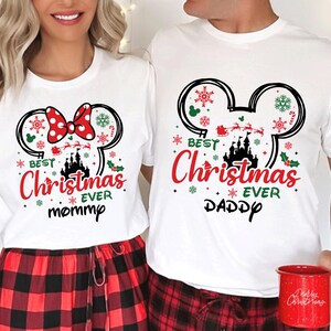 May include: Two white short-sleeve t-shirts featuring a black Mickey Mouse ear silhouette filled with red and green Christmas icons, a castle, and Santa's sleigh. The text reads "BEST Christmas EVER" with "mommy" on one shirt and "DADDY" on the other.